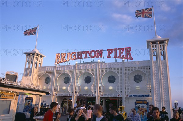 ENGLAND, East Sussex, Brighton, Brighton Pier with groups of people in the foreground.