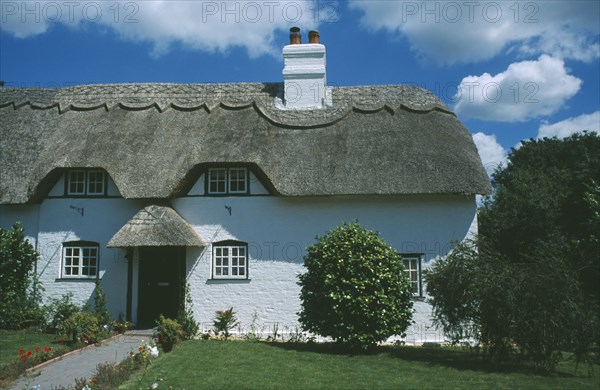 ENGLAND, Hampshire, Lyndhurst, Thatched Cottage seen from across green front lawn.