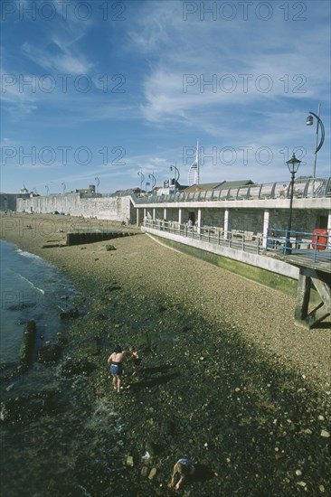 ENGLAND, Hampshire, Portsmouth, Old Portsmouth. Family playing amongst rocks on stretch of shingle beach next to walls.