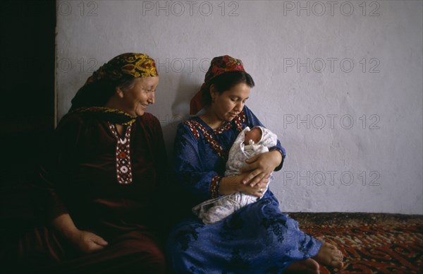TURKMENISTAN, Ashkhabad, Women in traditional dress with baby at home.