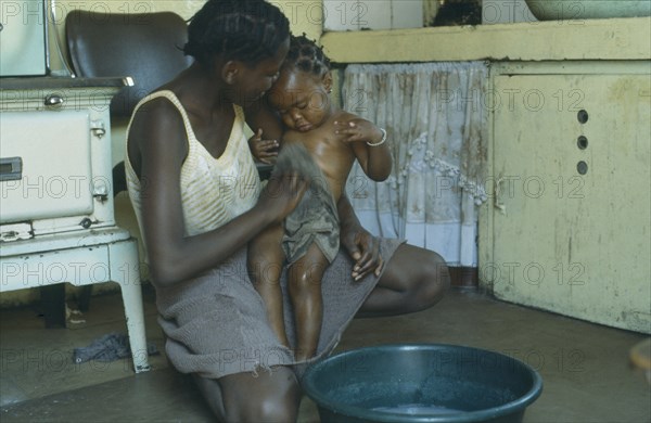 SOUTH AFRICA, Children, Bathing, Mother bathing baby daughter inside home.