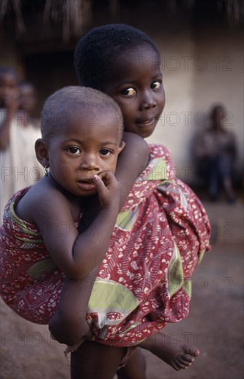 GHANA, Volta Region, Hohoe, Young girl looking after little sister carried on her back.