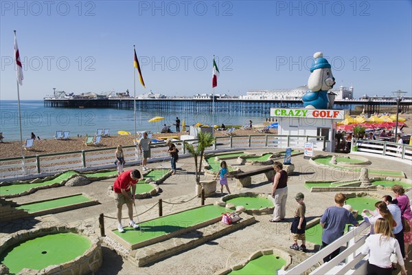 ENGLAND, East Sussex, Brighton, Tourist family playing crazy golf on the seafront with Brighton Pier beyond