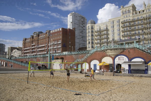 ENGLAND, East Sussex, Brighton, Young men playing Volleyball on the lower esplanade. Seafront Hotel buildings behind.