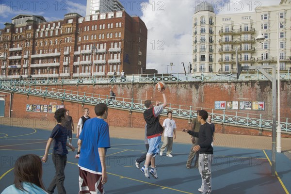 ENGLAND, East Sussex, Brighton, Young men playing Basketball on the lower esplanade. Seafront Hotel buildings behind.