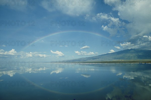 TANZANIA, Lake Natron, Reflected rainbow bisected by a pink line of flamingoes feeding in the algae rich waters of large soda lake.