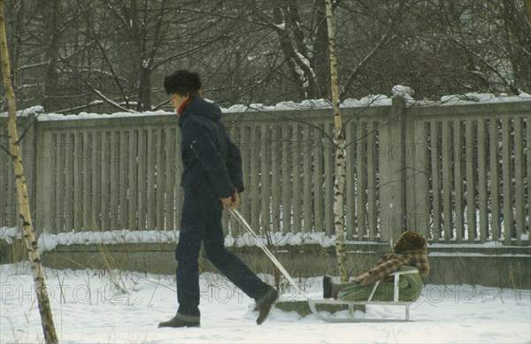 Russia, Moscow, "Father pulling child on sledge through the snow, both wrapped up against the cold."