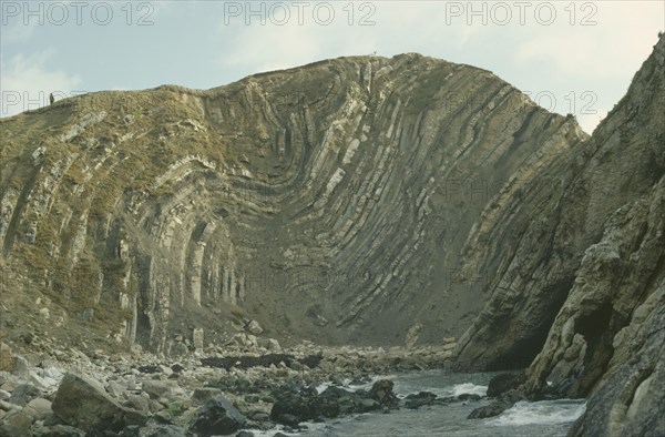 ENGLAND, Dorset, Coastal limestone cliffs with clearly defined folds.  Figure standing on top.
