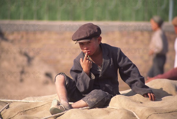 CHINA, Xinjiang Province, Kashgar,  Tajik boy sat on sacks