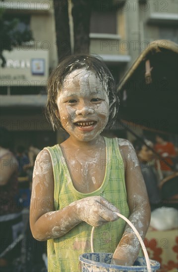 THAILAND, Bangkok, "Young girl with bucket, covered in mud at the Songkhran Festival. Thai New Year, 15 April."