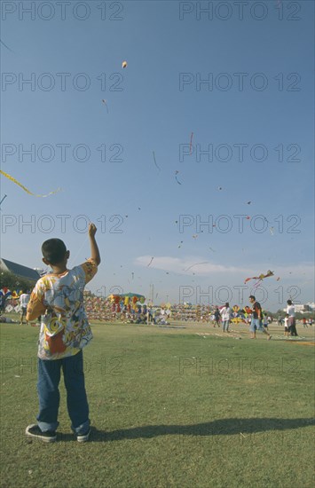 THAILAND, Bangkok, "Kite festival at Sanam Luang, February. Boy flying one in foreground, many others in sky."