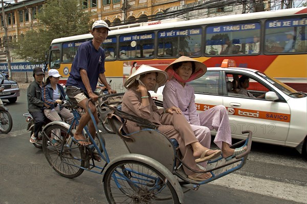 VIETNAM, South, Ho Chi Minh City, Passengers riding in a cyclo in heavy traffic down a busy street