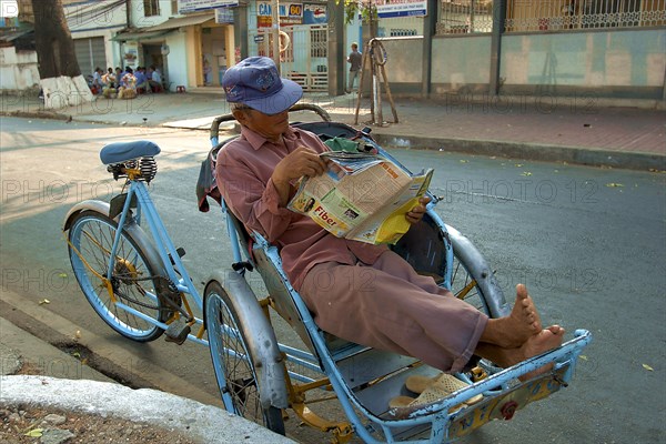 VIETNAM, South, Ho Chi Minh City, A Cyclo driver reading a magazine taking a break