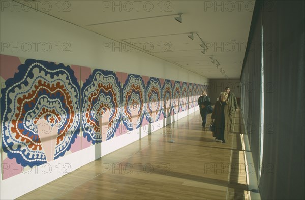 ENGLAND, East Sussex, Bexhill on Sea, De La Warr Pavilion. Interior view of exhibition space with a colourful art display on walls and visitors walking through.