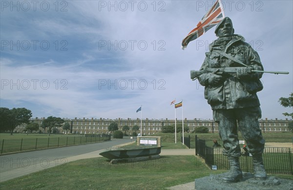 ENGLAND, Hampshire, Portsmouth, Royal Marines Museum. Large statue of a Royal Marine holding gun on display in front of building and Union Jack flag flying behind.