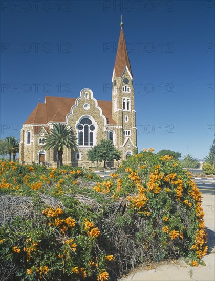 NAMIBIA, Windhoek, Christuskirche church exterior viewed from Parliament Gardens with a flowering bush in the foreground.