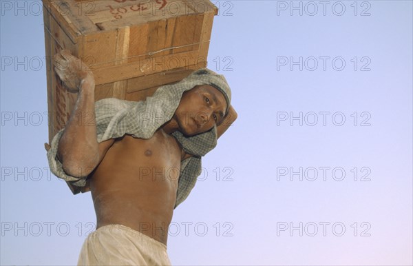 MYANMAR, Mandalay Dock, "Man carrying a crate above his head, wearing head scarf. Banks of the Irrawaddy"