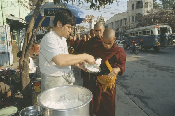 MYANMAR, Mandalay , Giving early morning Alms to young Monks queuing up at side of road.