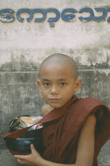 MYANMAR, Kawthoung, Young novice monk with bowl full of Alms offerings.