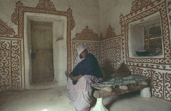 MAURITANIA, Oulata, Woman in interior of traditional mud house with decorative painted design on walls.