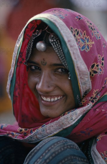 INDIA, People, Head and shoulders portrait of a smiling woman wearing pink sari with flower print and traditional jewellery.