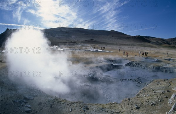 ICELAND, Namafjall, Hverir. High temperature geothermal area. Steam rising from the hot springs with visitors on the ground and mountains in the distance.