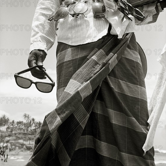 INDIA, Kerala, Kovalam Beach, A sunglass-seller displays his wares on a tourist beach in southern India.