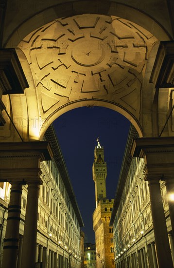 ITALY, Tuscany, Florence, Palazzo Vecchio framed by arch of Loggia Medici and Galleria Uffizi at night.