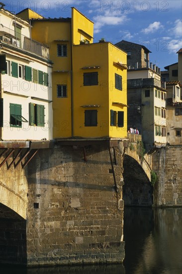 ITALY, Tuscany, Florence, Ponte Vecchio.  Buildings on bridge above the River Arno with people sitting on wall.