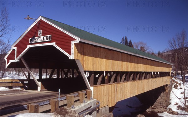 USA, New Hampshire, Jackson, "Wooden covered bridge over water, snow on the ground."