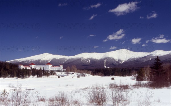 USA, New Hampshire, Bretton Woods, "Mount Washington Hotel, large white building with red roof, snow peaked mountain range behind."