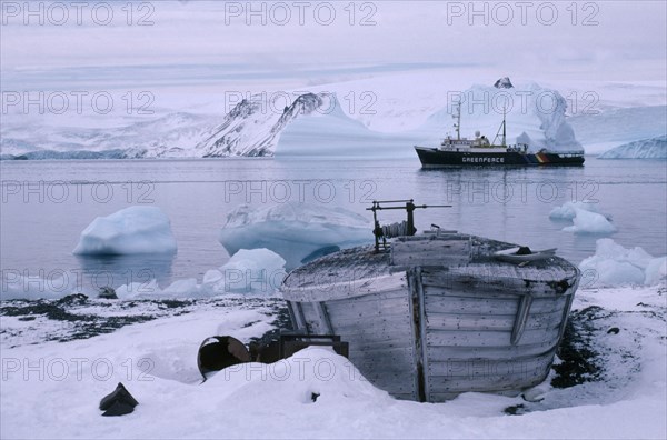 ANTARCTICA, King George Island, Old whale boat on land with Greenpeace ship in distance.