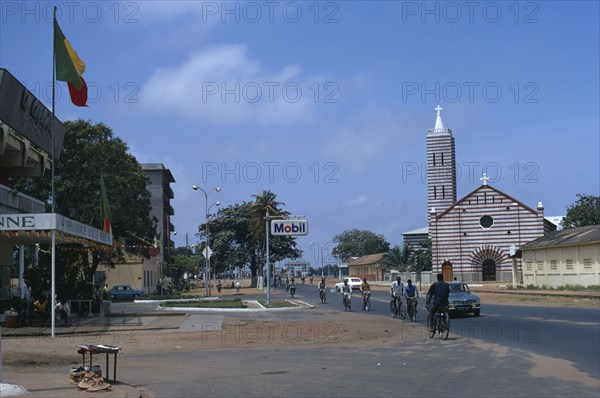BENIN, Cotonou, Street scene with church and passing cyclists and cars.