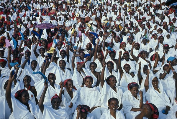 SOMALIA, Politics, Independence Day Parade. A mass of seated women with their arms raised in the air dressed in white with multi coloured headscarfs.