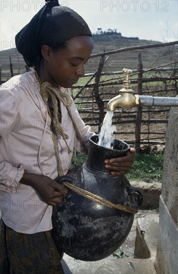 ETHIOPIA, South Wollo, Woman filling water vessel from tap of protected spring water source.