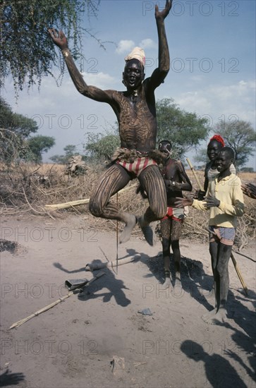 SUDAN, Tribal People, Dinka tribesman with his body painted with ash leaping in to air with his arms held in the shape of the horns of a bull during dance