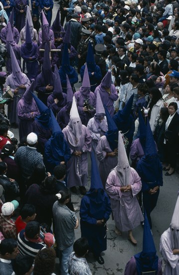 ECUADOR, Quito, Good Friday procession in Plaza San Francisco.  Penitents wearing purple robes and hoods walk through crowds.