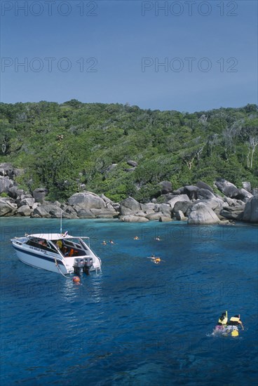 THAILAND, Similan Islands, Ko Bangu, Snorkelers in the water next to a small motor boat near the rocky shore.
