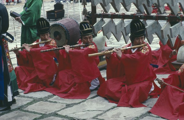 SOUTH KOREA, Religion, Buddhism, Confucian Rites Orchestra. Line of men in red robes sat on ground playing bamboo flutes