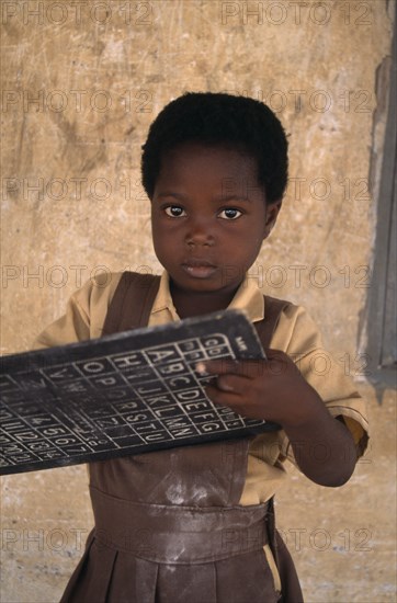 GHANA, Education, Portrait of pupil from primary school in village near Accra holding small blackboard printed with alphabet and numbers.