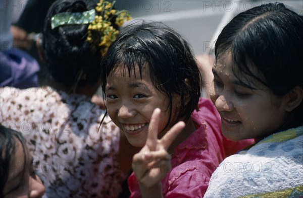 MYANMAR, Mandalay, Young girl smiling and making the V peace sign with fingers amongst other girls at water festival