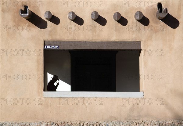 USA, New Mexico, Santa Fe, Detail of the Palace of The Governors in the Plaza with a man wearing a cowboy hat walking under the pueblo style arches