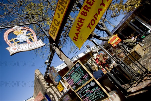 USA, New Mexico, Santa Fe, The Cowgirl Cafe outdoor eating area with customers and a waiter. Sign showing the days meals