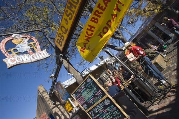 USA, New Mexico, Santa Fe, The Cowgirl Cafe outdoor eating area with customers and a waiter. Sign showing the days meals