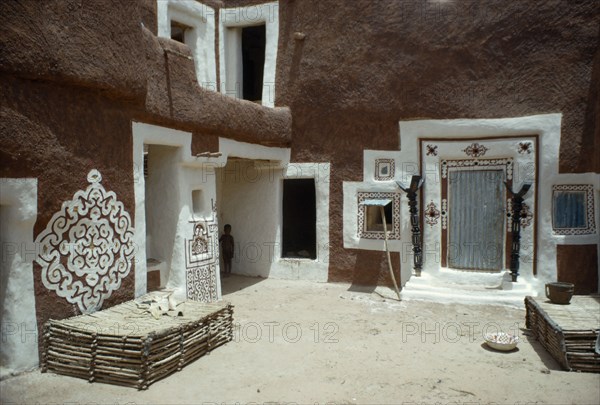 MAURITANIA, Oualata, "Traditional mud architecture decorated with bas relief motifs of applied gypsum, white and red clay.  Small child standing in shadow of corner of building. "