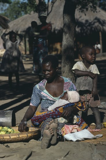 ZAMBIA, Ukwimi Settlement, Mozambique refugee woman and children with basket of fruit.