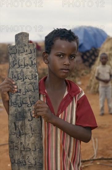 KENYA, Mandera, Somali refugee camp run by UNHCR.  Young boy attending Koranic school holding piece of wood inscribed with Koranic script.