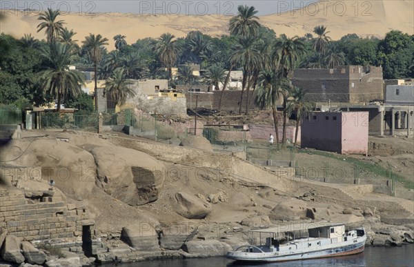 EGYPT, Nile Valley, Elephantine Island, "Oldest inhabited part of Aswan, flat roof houses amongst palm trees and boat moored against shore."