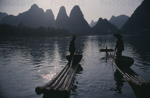 CHINA, Guangxi Province, River Li, Cormorant fishermen silhouetted on stretch of river in the Guilin area with limestone peaks behind.