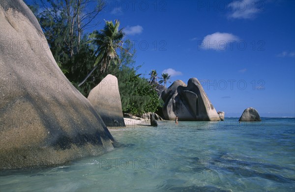 SEYCHELLES, La Digue , Anse Source D Argent, Rock formations along the coast with a woman bather walking into the turquoise sea